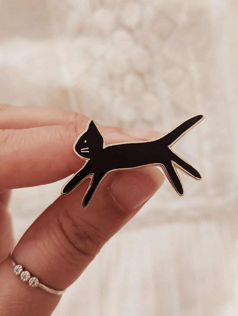 Hand holding black kitty enamel pin made of gold tone brass, 38mm size, designed in Montreal Canada