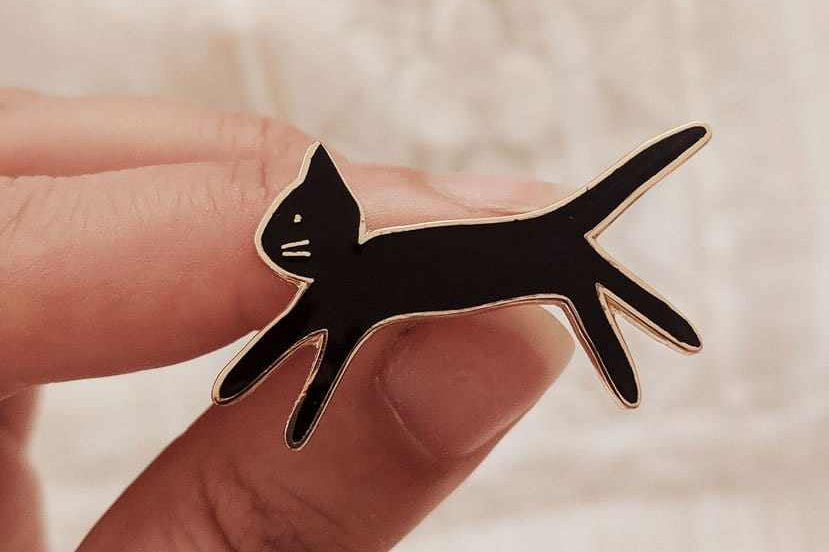 Hand holding black kitty enamel pin made of gold tone brass, 38mm size, designed in Montreal Canada