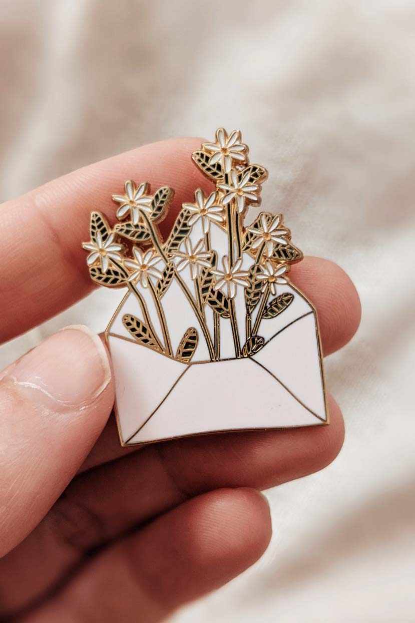Une main tient cette délicate épinglette Lettre pleine de fleurs, signée Mimi & August