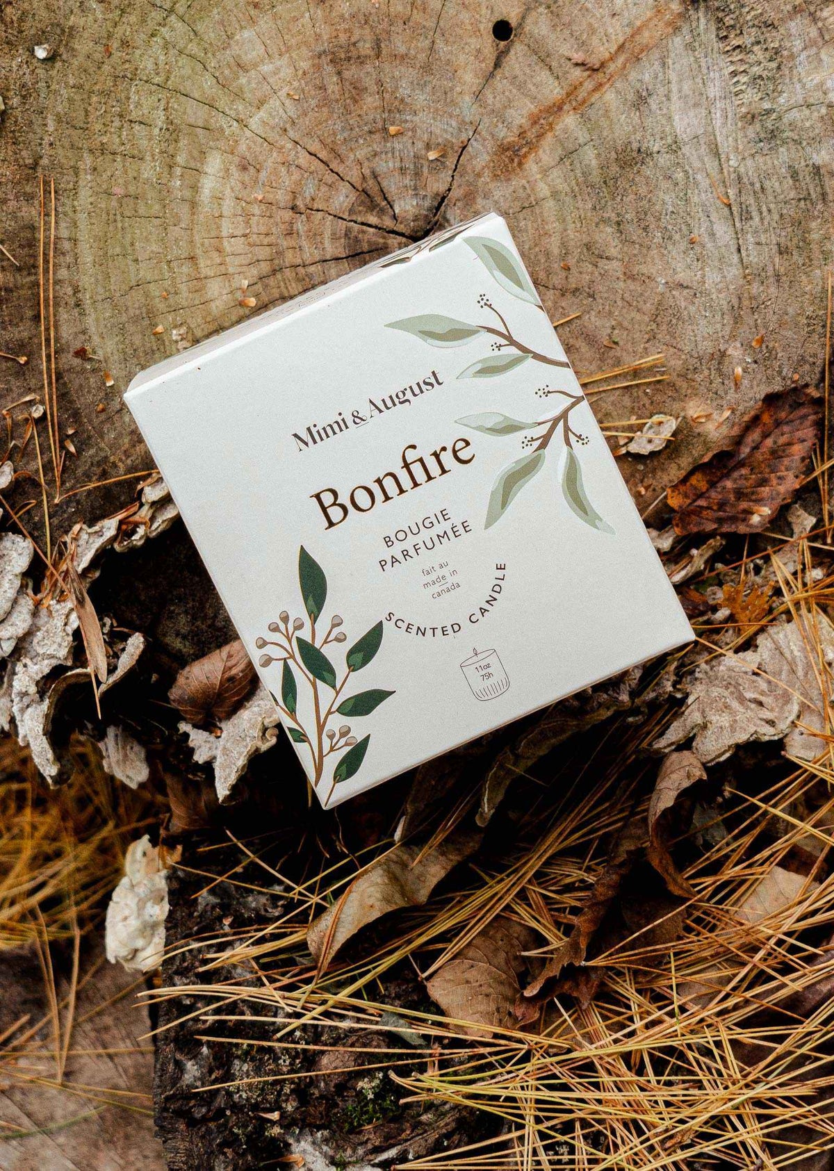Bonfire campfire candle packaging on rustic wood with dried leaves and pine needles