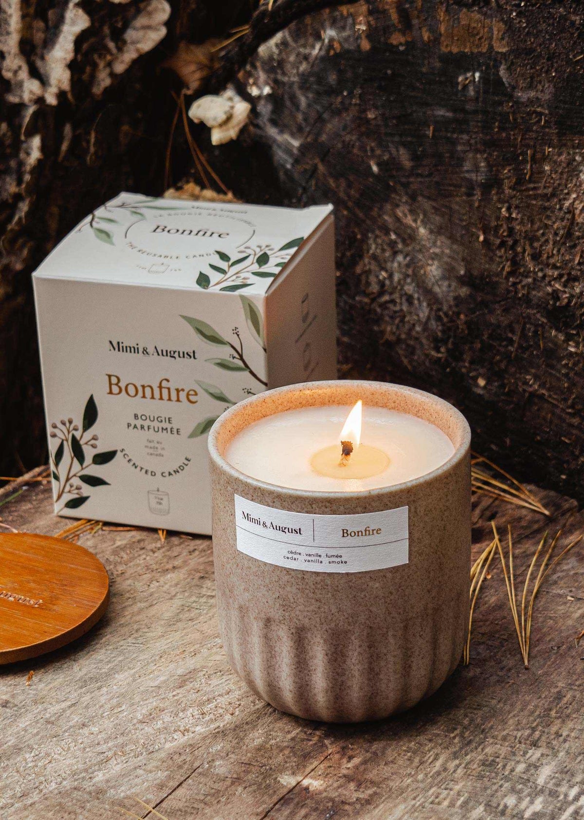 Lit Bonfire reusable soy campfire candle in ceramic cup with packaging on wooden surface outdoors