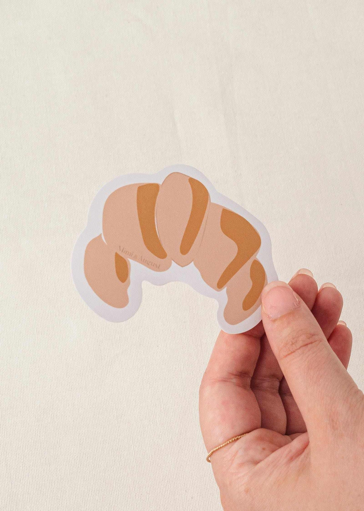 Hand holding croissant vinyl sticker with matte finish and white border