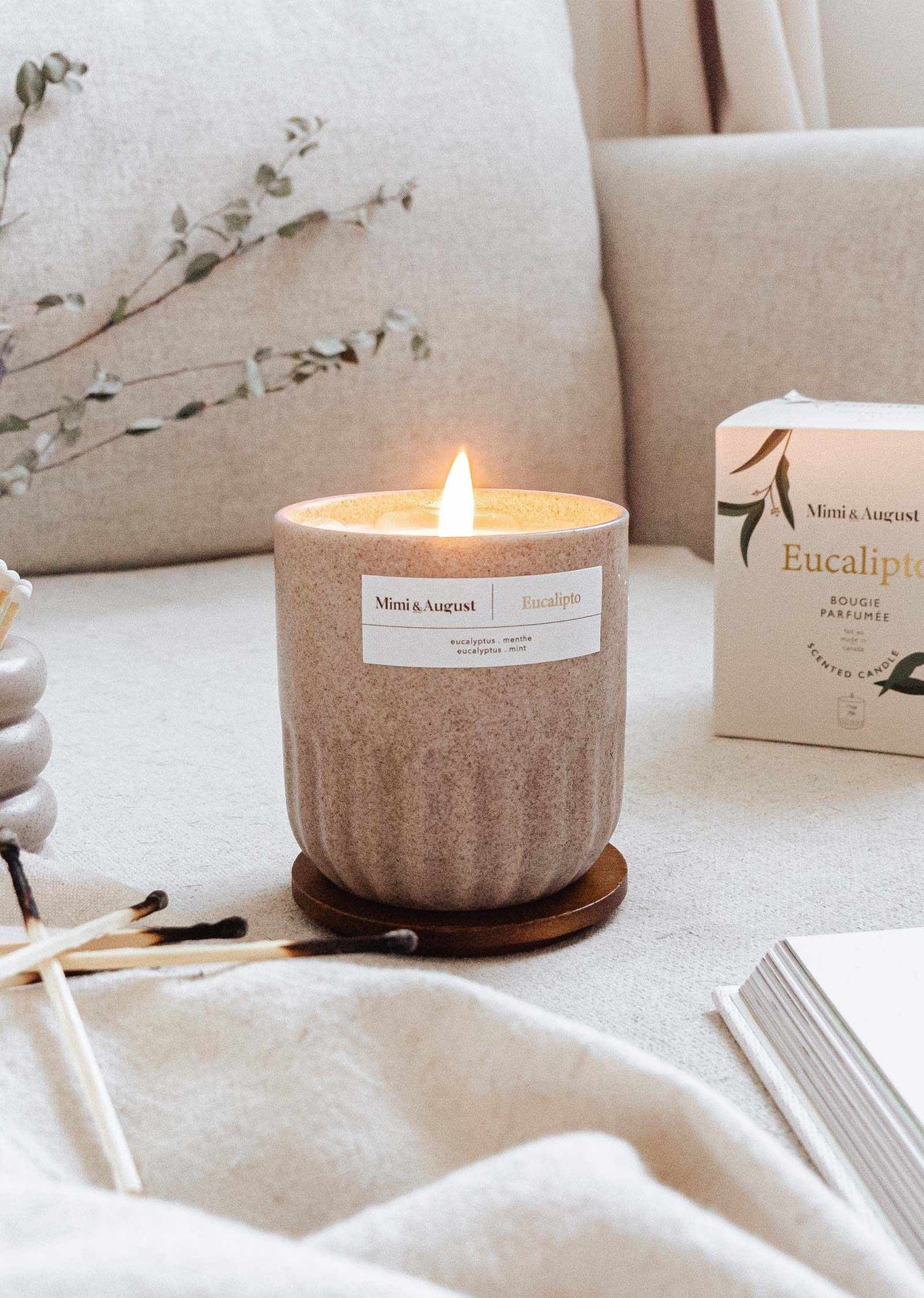 Lit eucalyptus candle in a reusable ceramic cup on a cozy surface with eucalyptus leaves in the background
