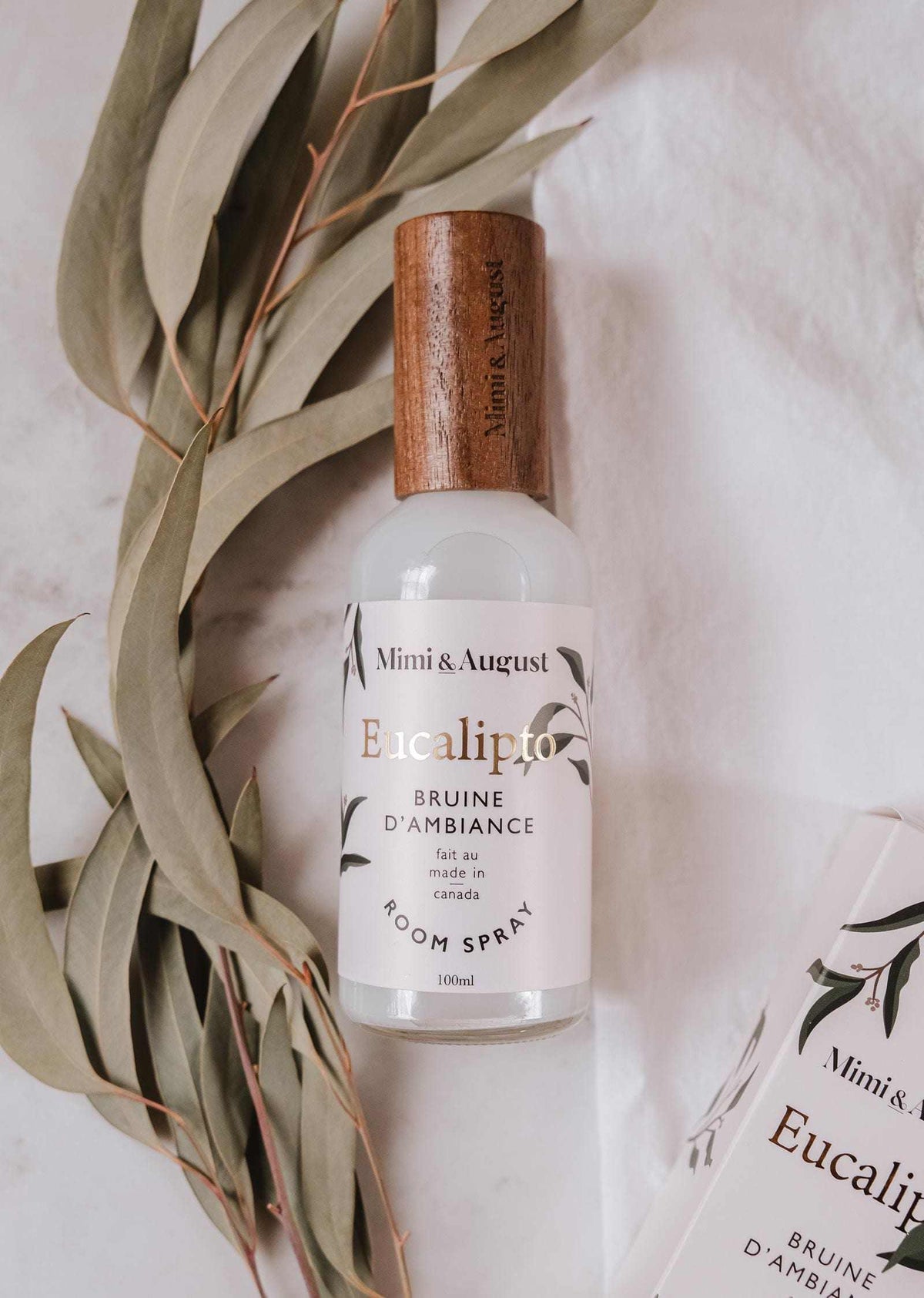 Eucalyptus room spray bottle with wooden cap beside eucalyptus leaves on white fabric background