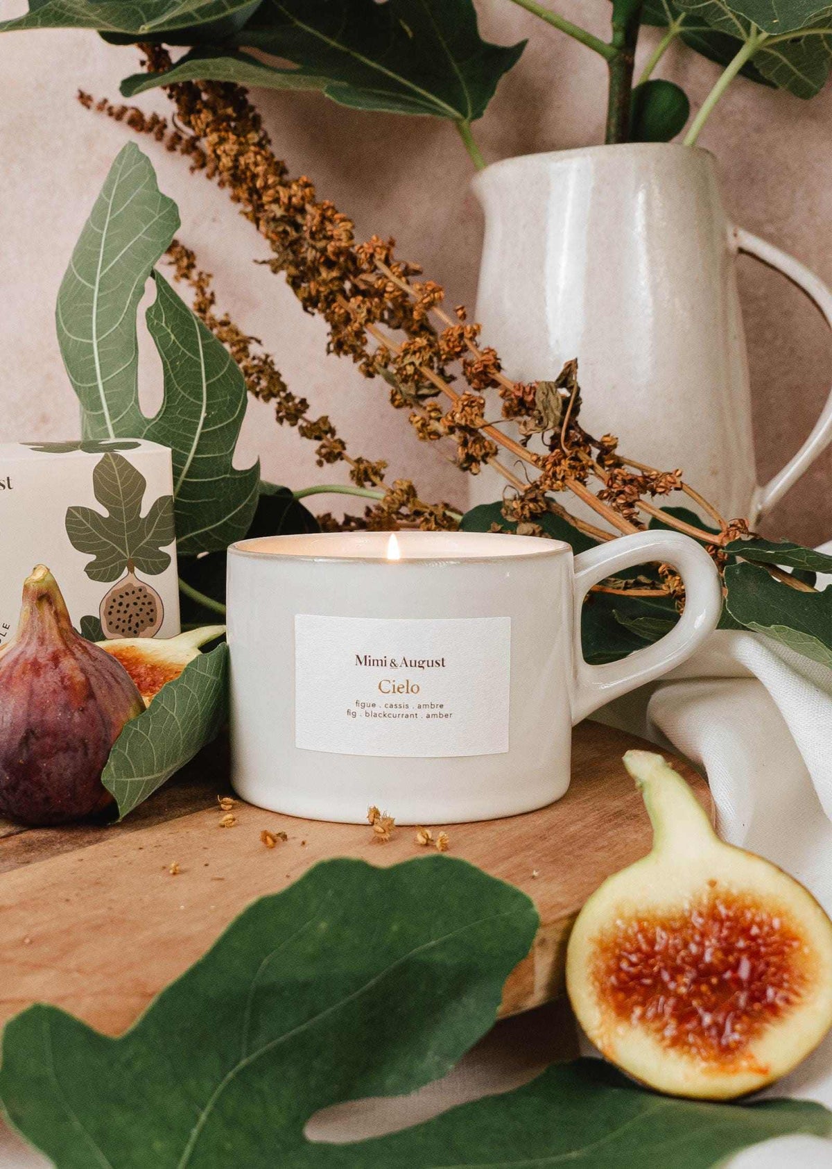 Fig candle in a reusable ceramic cup with fresh figs and greenery on a wooden surface.