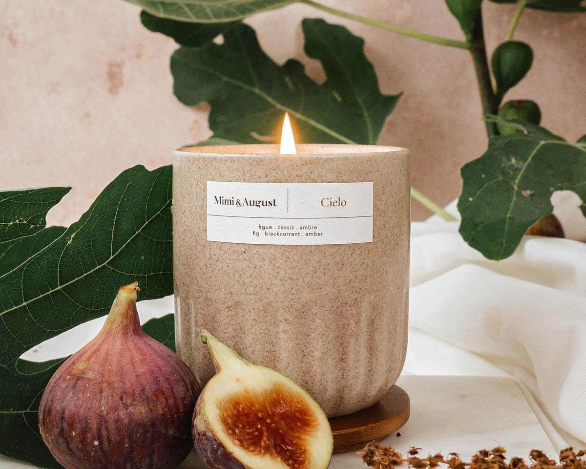 Burning fig candle in a textured cup with figs and green leaves background