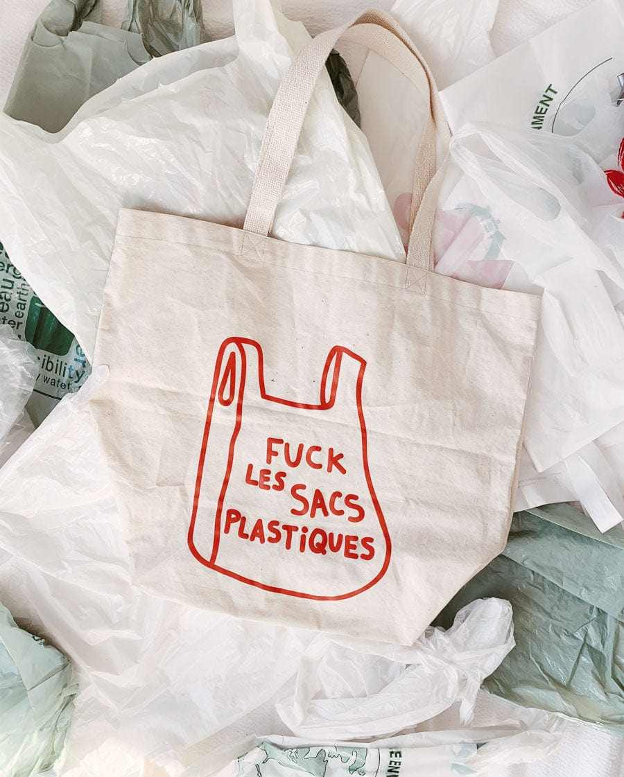 Natural tote bag with "Fuck les sacs plastiques" text, eco-friendly reusable cotton design against plastic bags background