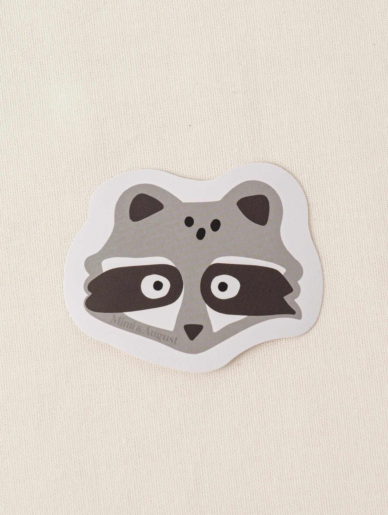 Cute vinyl sticker of a raccoon face with matte finish and white border