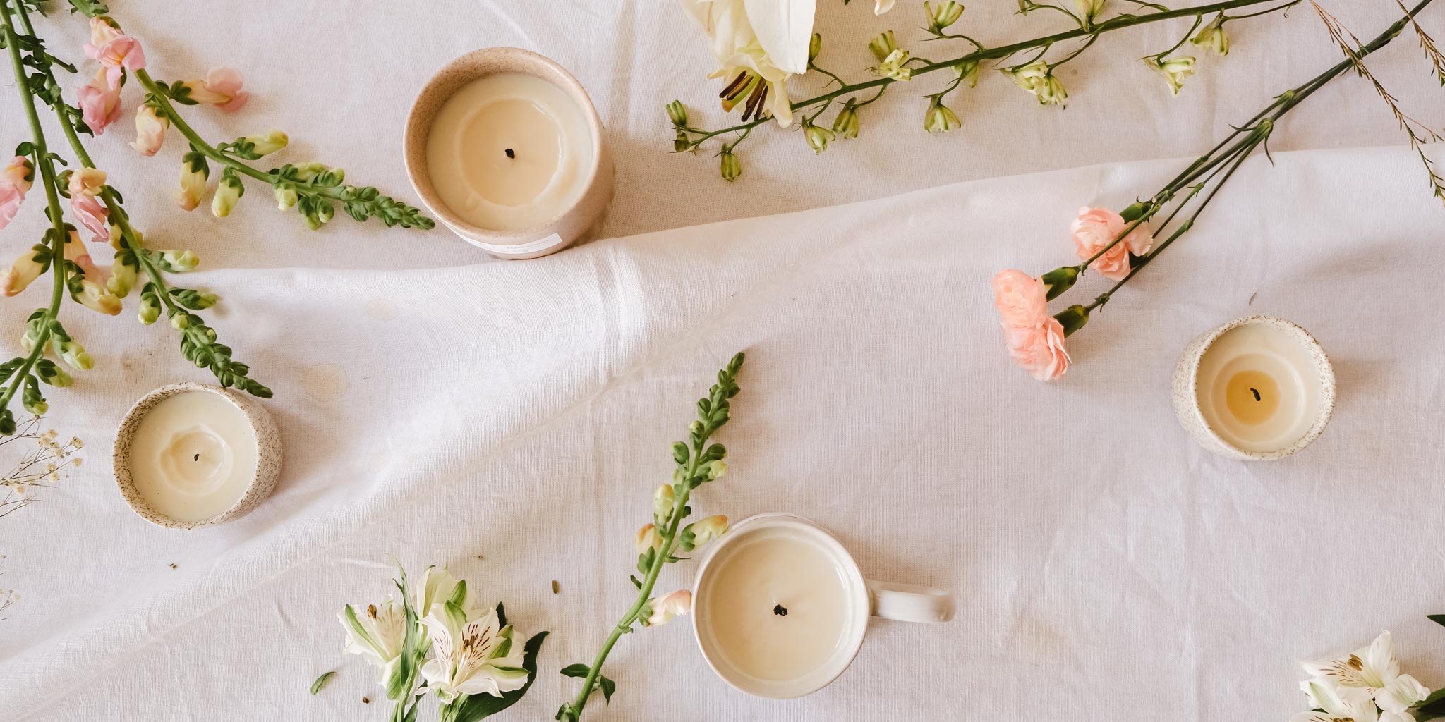 Floral scented candles laid on the ground beside flowers 