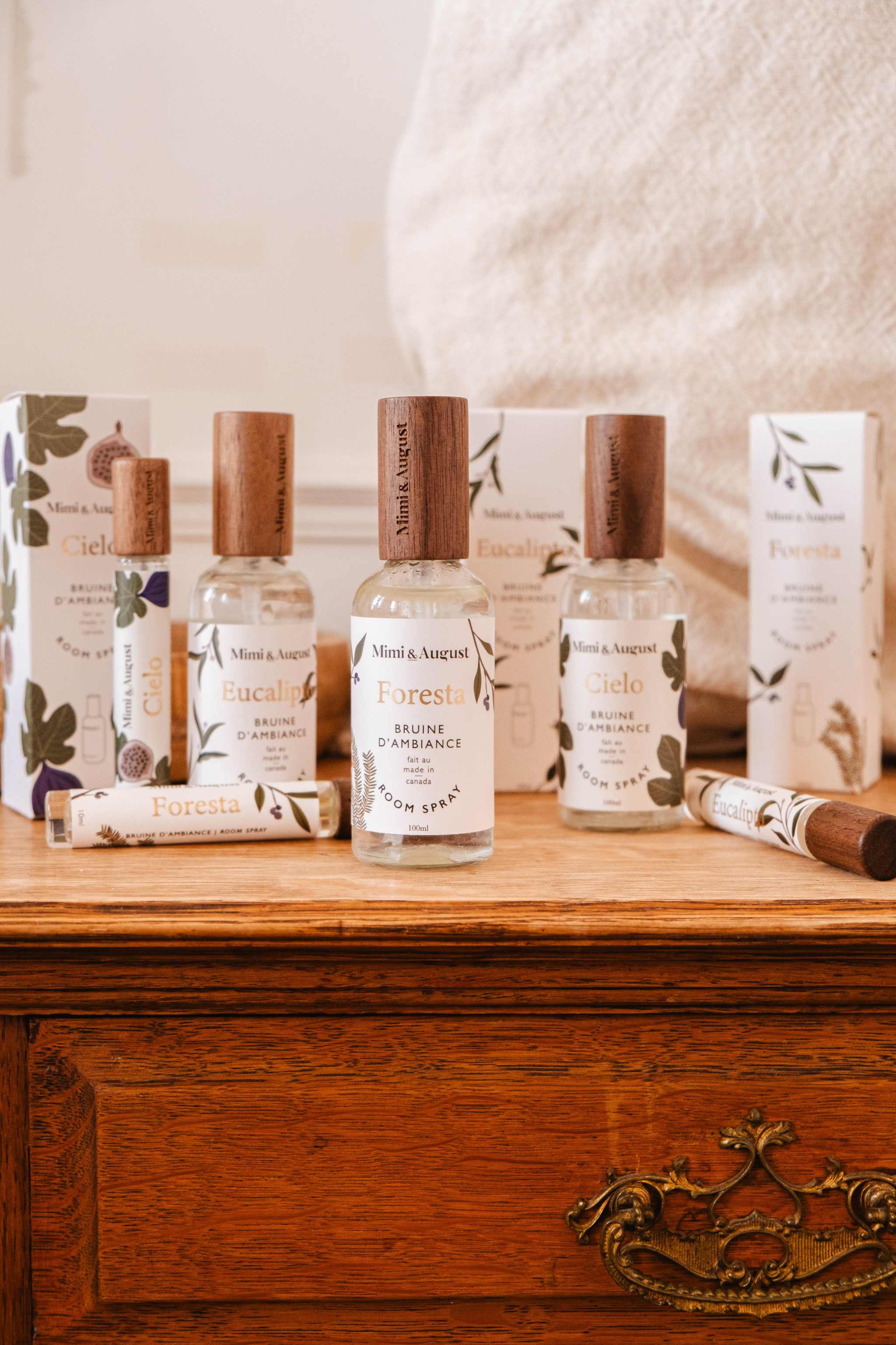 A collection of Mimi & August room sprays and packaging boxes arranged on a wooden dresser.