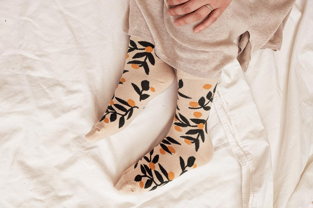 A person laying on a bed wearing socks with orange leaves.