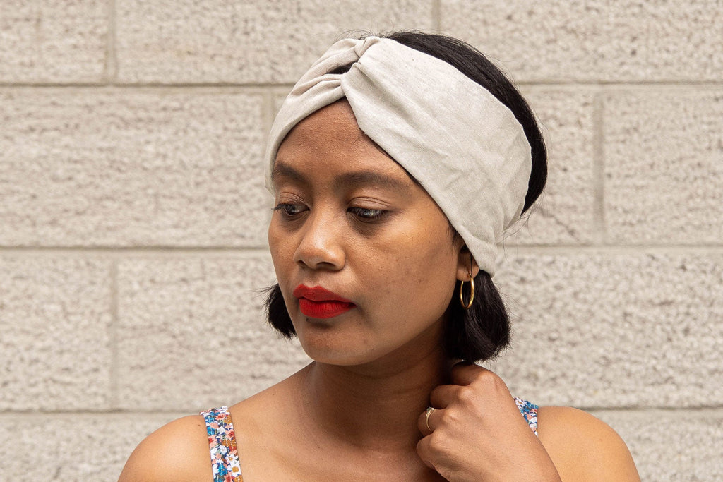 A woman with a headwrap looking to the side against a brick wall background.