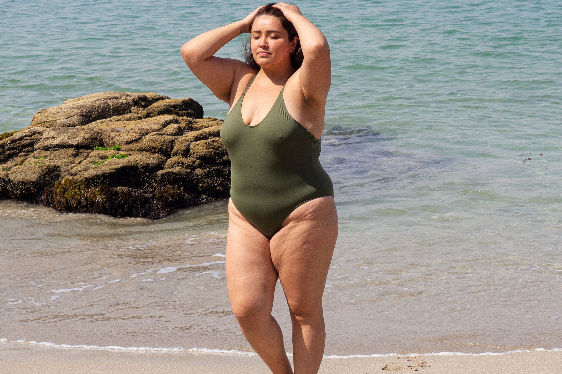 A woman in a green swimsuit standing on a beach.