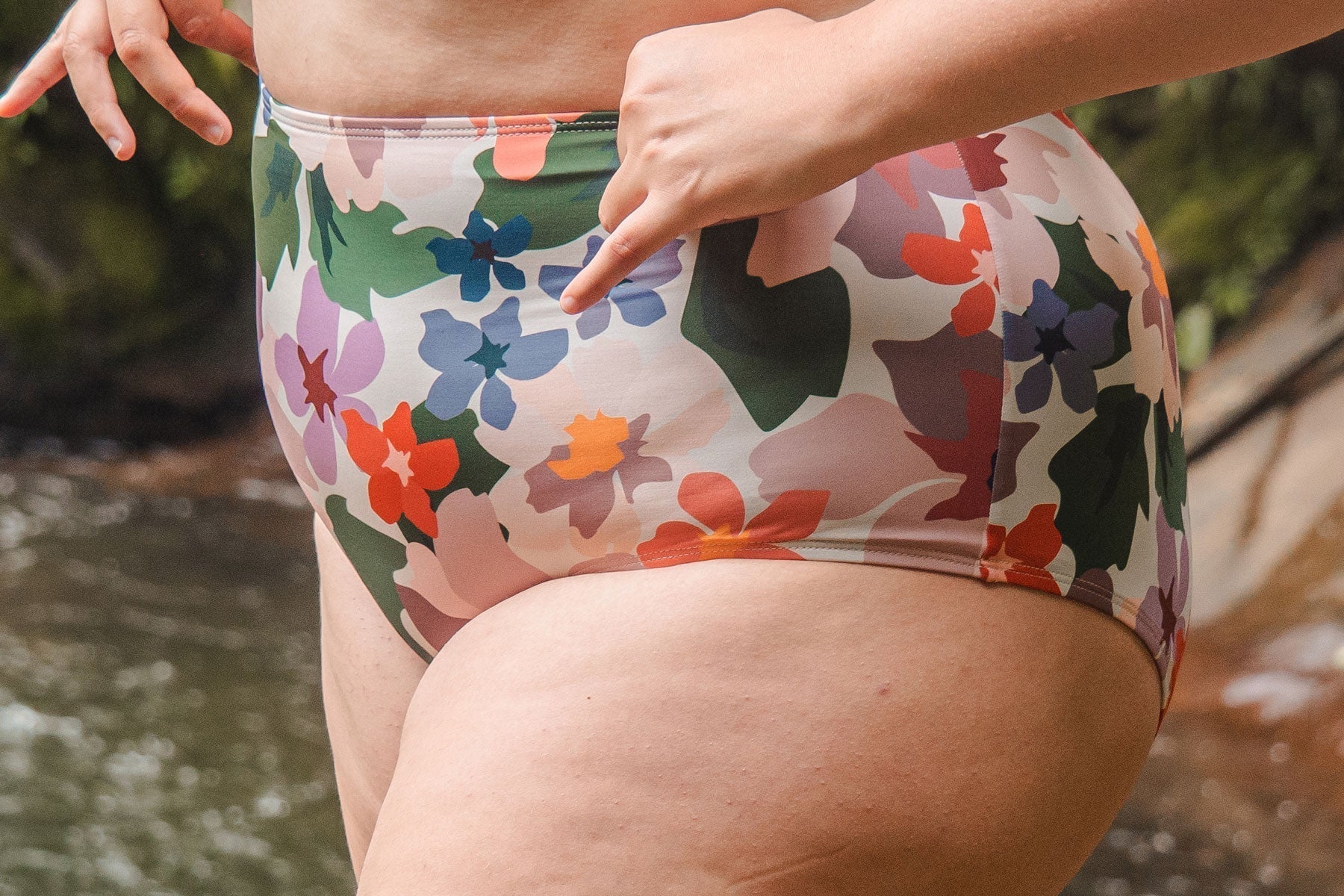 A woman in a floral print bikini standing by a river.