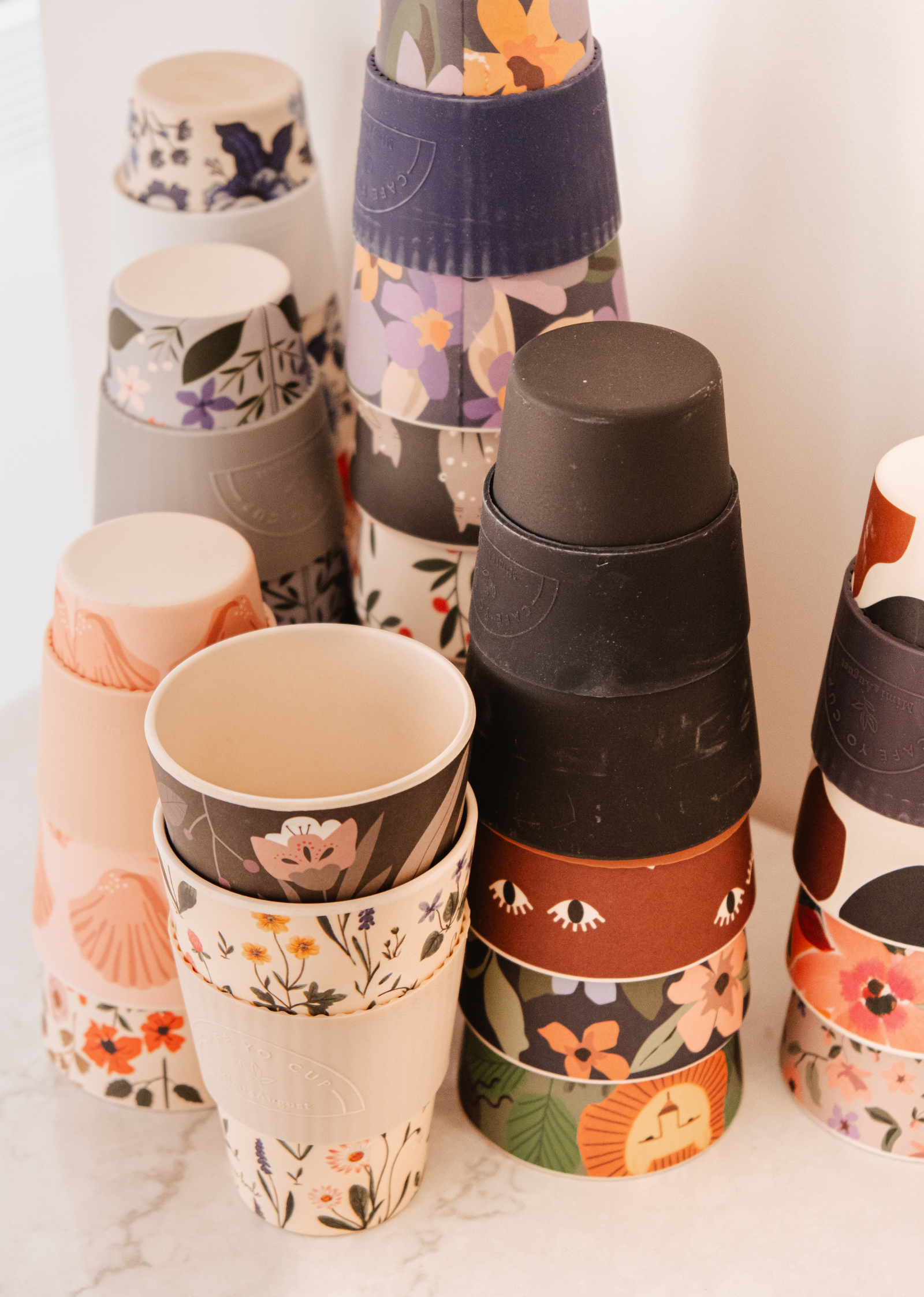 Un groupe de Defect Café Yo Cups avec différents motifs, y compris un couvercle en silicone par Mimi & August.