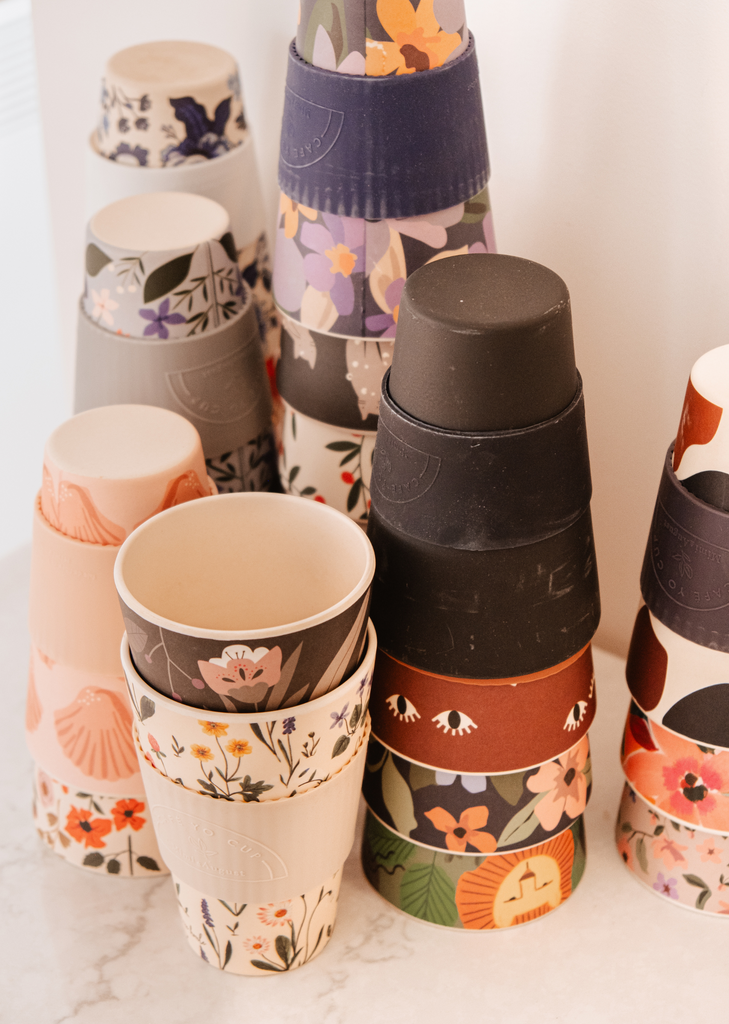 A group of Defect Café Yo Cups with different designs on them, including a silicone lid by Mimi & August.