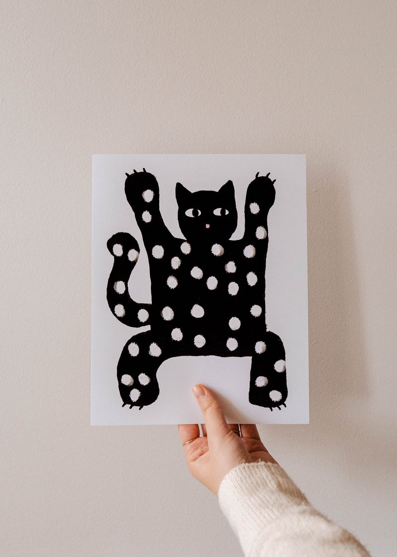 Un amoureux des chats brandissant une reproduction artistique de haute qualité d'un chat noir qui fait peur de Mimi & August.