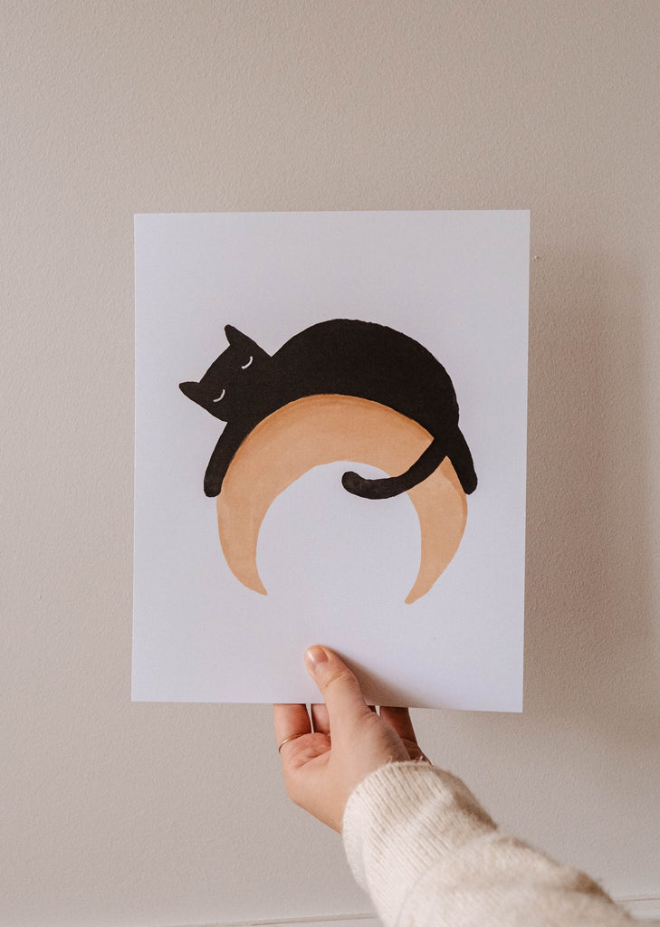 A person holding up a Black Cat on a moon Crescent Art Print by Mimi & August.