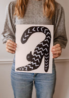 A woman holding up a Stretchy Black Cat Art Print by Mimi & August in a yoga-like posture.