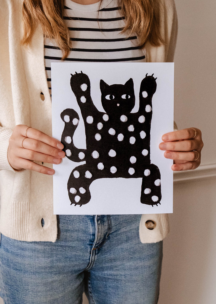 A cat lover proudly holds up a Mimi & August Scary Black Cat Art Print.