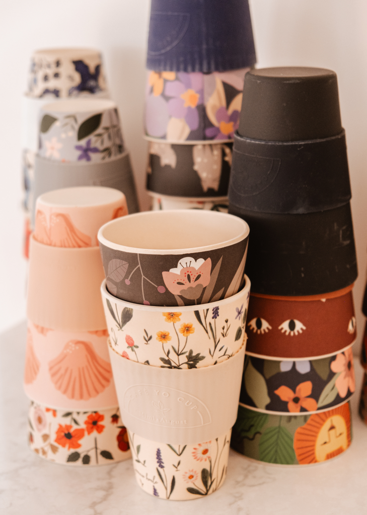 Une pile de gobelets Mimi & August Defect Café Yo Cups avec différents motifs, y compris des options recyclables.