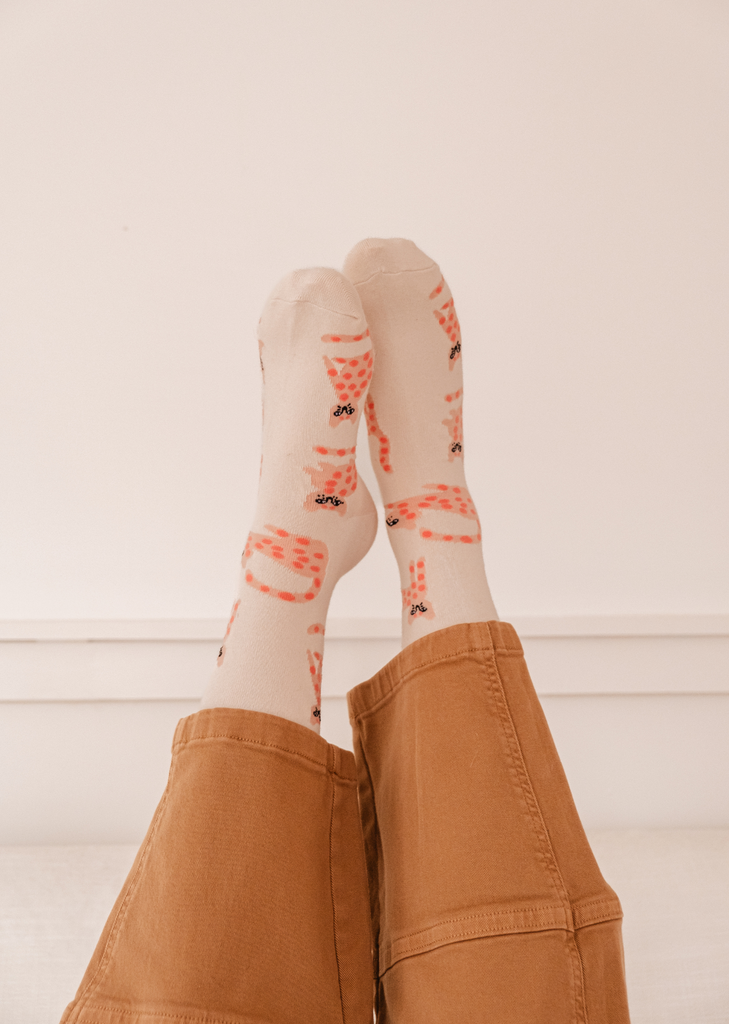 The comfortable legs of a cat lover adorned in Leo The Cat Socks by Mimi & August, with a cute feline design.