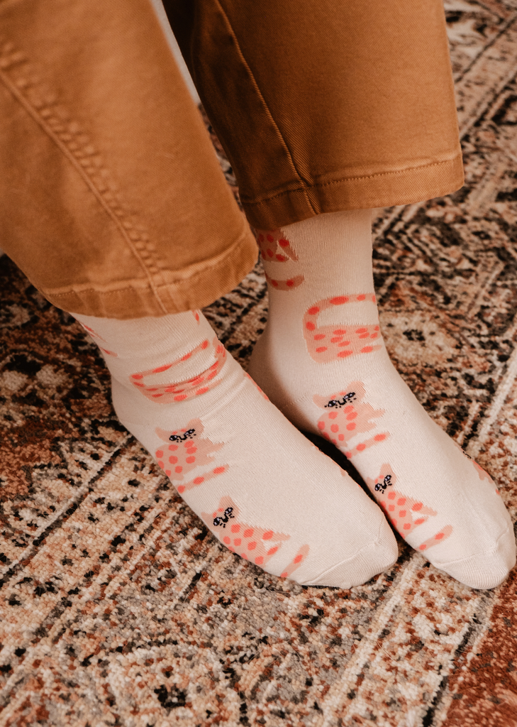 A woman's feet on a rug wearing Mimi & August's Leo The Cat Socks.