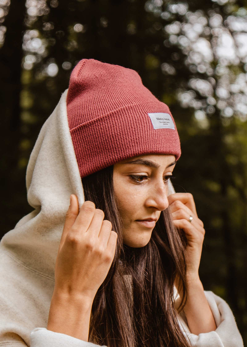 A woman wearing a pink mimi and august Astro Beanie in the woods.