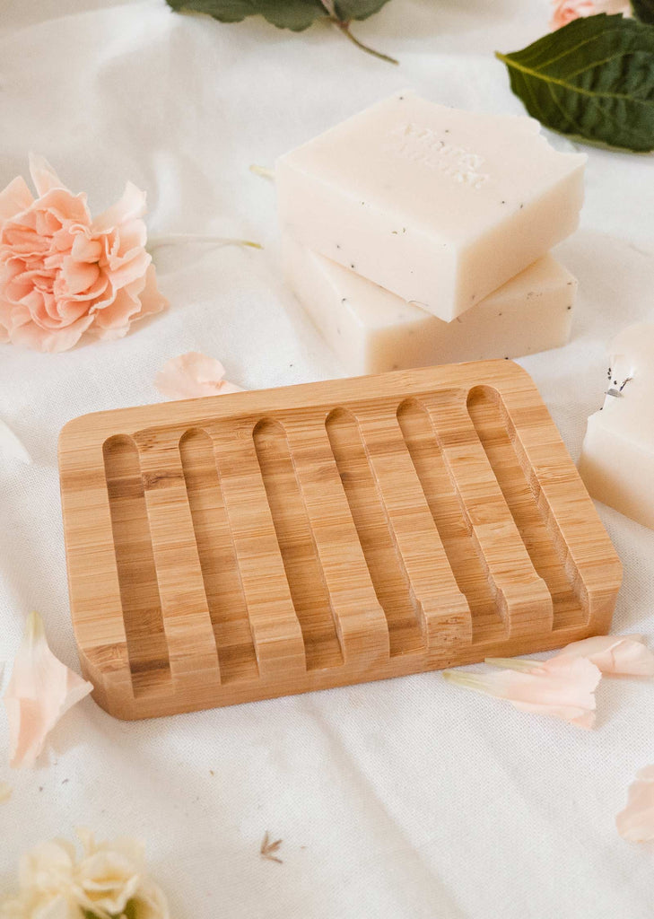 A durable mimi and august Bamboo soap dish with soaps and flowers on a table.