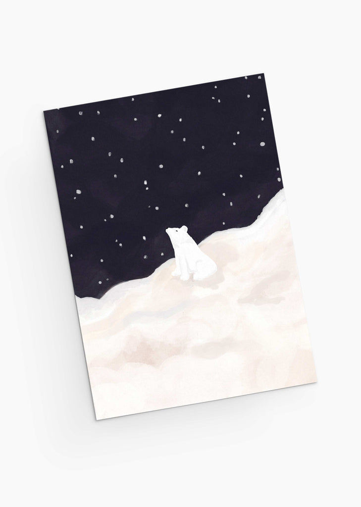 L'illustration d'un ours blanc assis sur un sol enneigé sous un ciel étoilé capture le charme douillet des cartes de vœux de Noël dans la collection "Ours sous les étoiles" de Mimi & August.