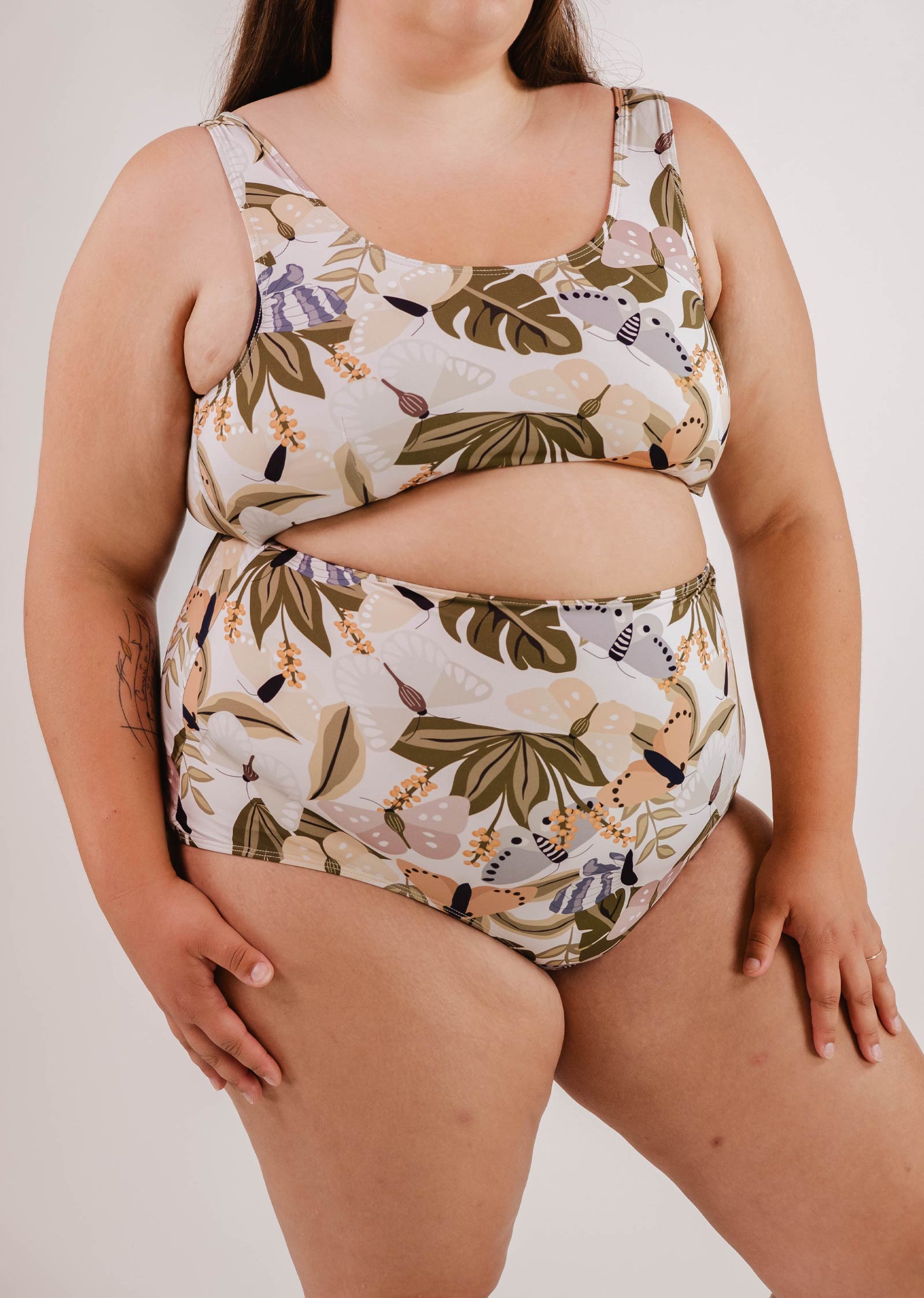 A woman wearing a matching, patterned, Bermudes Mariposa extra high waisted bikini bottom by Mimi & August with a flattering silhouette stands against a plain, white background.