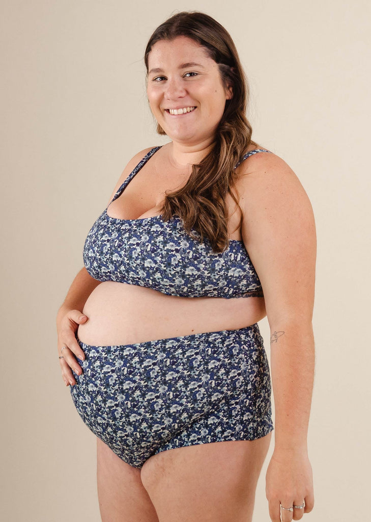 Une femme enceinte vêtue d'un bas de bikini taille extra haute à fleurs bleu Bermudes Moonflower de mimi et august.