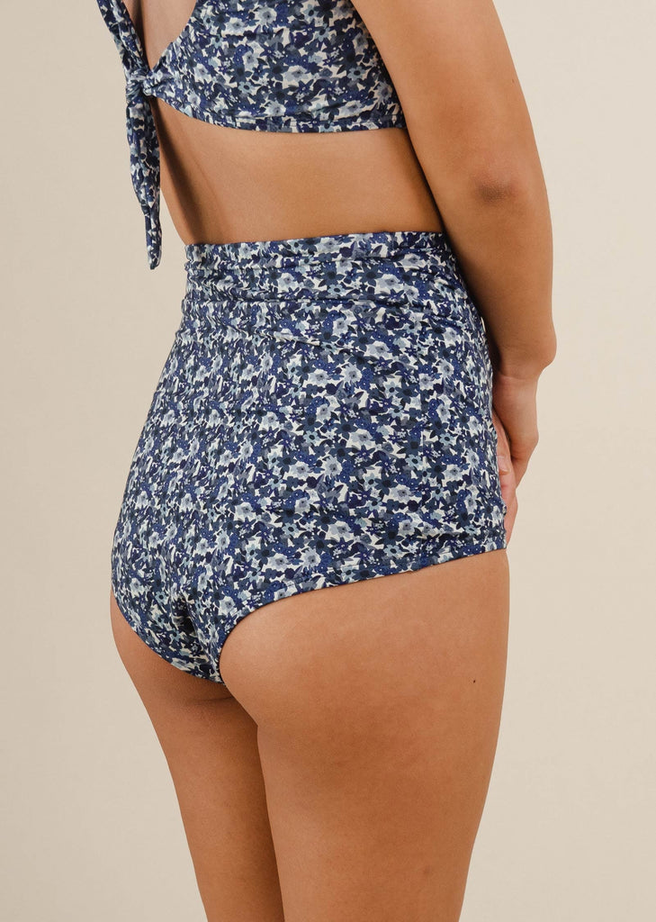 The back of a woman in Mimi and August's comfiest swimsuit with their blue floral High Waist Bikini Bottom.