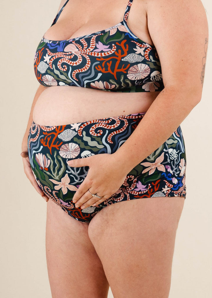 Une femme enceinte portant un bas de bikini taille extra haute Bermudes Oceana et un haut de bikini mimi et august.