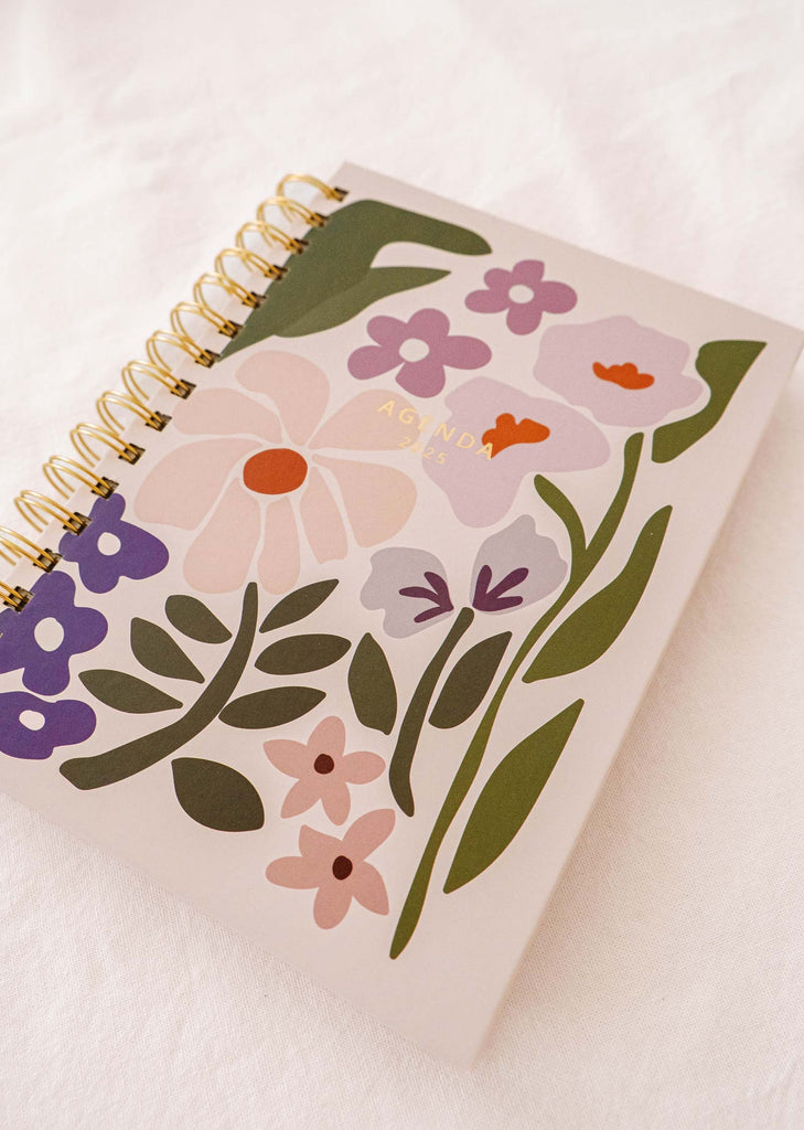 The Blooming - Agenda 2025 by Mimi & August is a spiral-bound notebook with a hand-illustrated floral cover, ideal for daily planning. Its striking design beautifully complements any white surface.