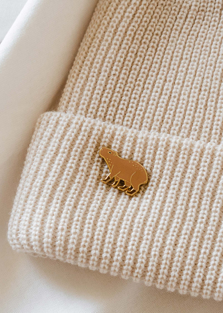 A Capybara enamel pin in a cream beanie by mimi and august