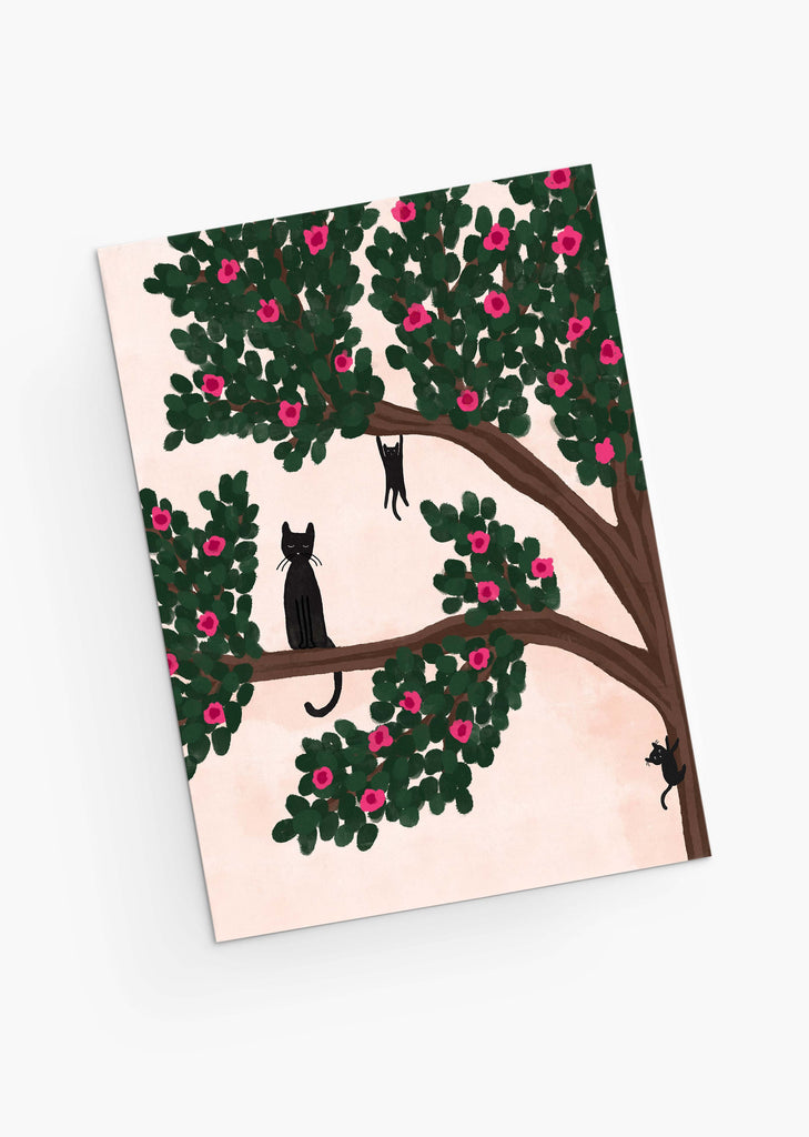 An illustration of a tree with green leaves and pink flowers, hosting two black silhouetted cats perched on its branches, displayed on a Mimi & August Mother's Day greeting card for a cat-loving mom.