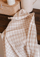Le linge en lin doux à carreaux beige et blanc est posé sur une surface en bois foncé à côté d'un panier tressé et d'un récipient en céramique.