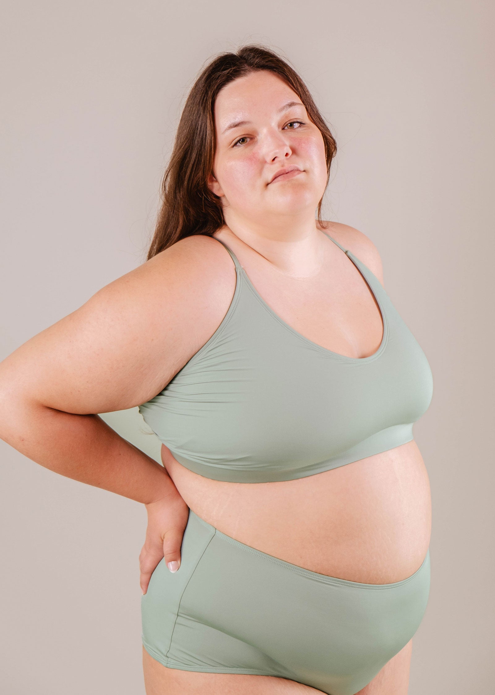 Woman wearing a green Chichi Agave Bralette Bikini Top from Mimi & August and matching leggings, standing with one hand on hip, neutral background.