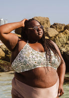 Une belle femme debout dans l'eau portant un haut de bikini mimi et august Chichi Herboria Bralette.