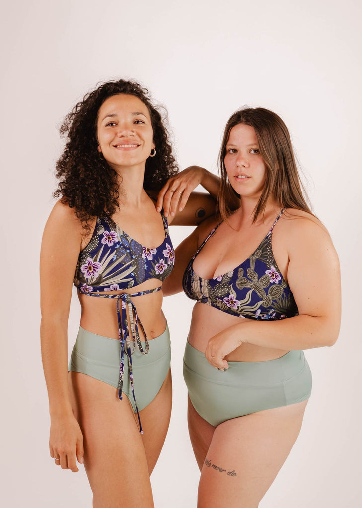 Two women pose together in Chichi Jardin de Nuit - Bralette Bikini Tops by Mimi & August with green high-waisted bottoms against a plain background, looking at the camera.