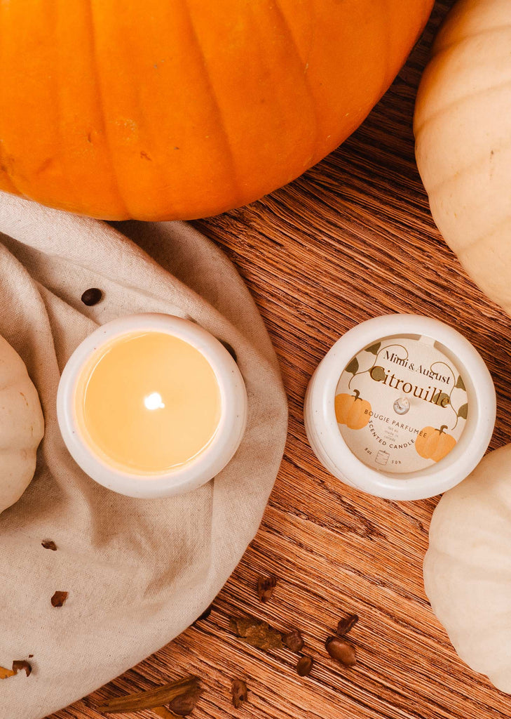A Pumpkin candle 8 oz with pumpkins and white pumpkins on a wooden table.