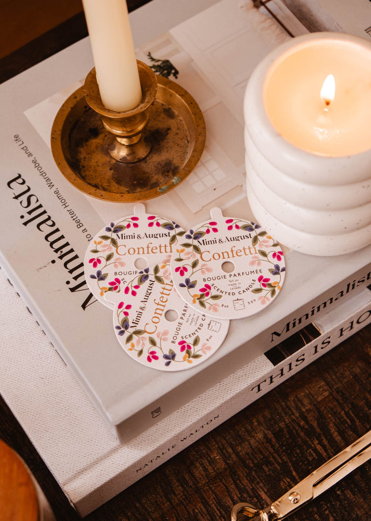 Une bougie réutilisable Confetti de Mimi & August et un livre sur une table, créant une atmosphère chaleureuse pour la célébration.
