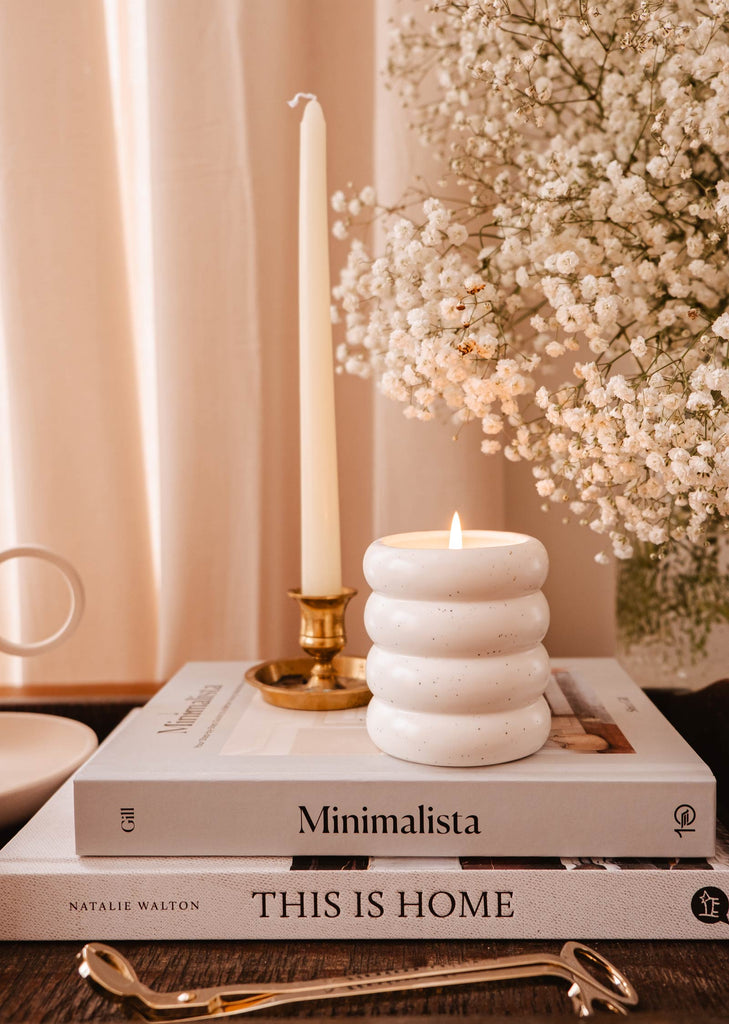 Une bougie réutilisable Confetti de Mimi & August est posée sur une table, au-dessus de livres.