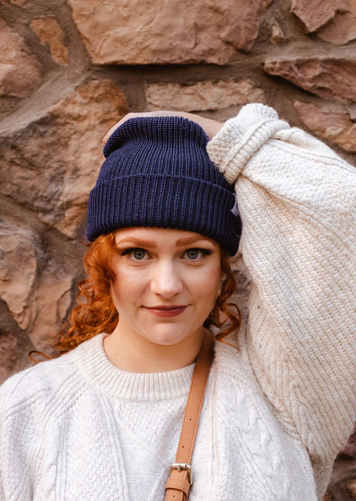 A woman wearing a Deep Blue Cuffed Beanie by mimi and august against a stone wall.