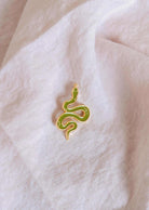 The Mimi & August Cute Serpent Enamel Pin in gold and green rests on a textured white fabric—an ideal gift for animal lovers.