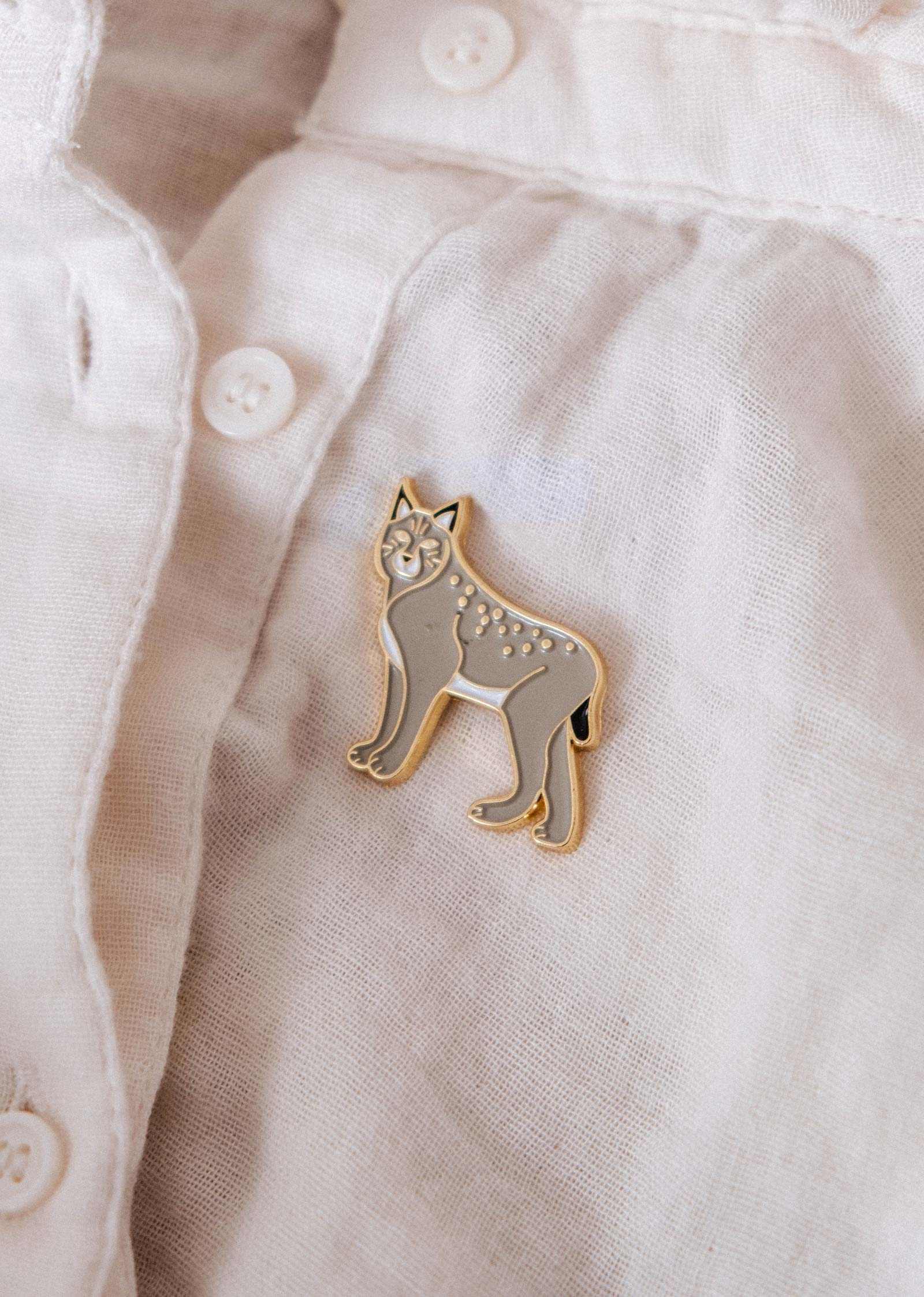 The Mimi & August Lynx Enamel Pin is displayed on a white button-up shirt, making it an ideal accessory for nature lovers and wildlife fans.