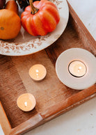 A wooden tray with a decorative plate, small pumpkins, and lit tealight candles sets the scene to showcase the Mimi & August Exclusive Discovery Kit—a must-have for exploring new fragrances.