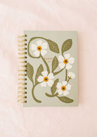 The Fields of Flowers - Agenda 2025 by Mimi & August showcases a robust cover adorned with a floral design of white blooms and vibrant green foliage, elegantly enhanced by a strong spiral binding.