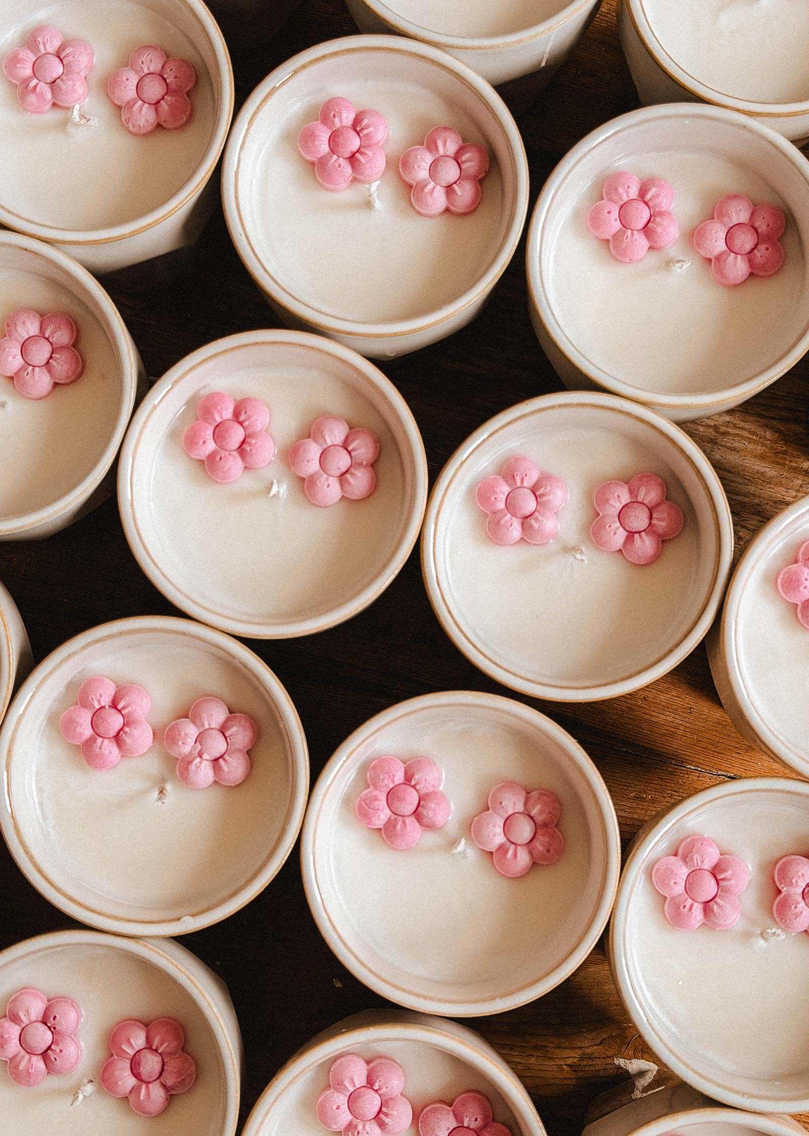 Mimi & August Special Edition Candle features a round white container, topped with two small pink flower-shaped wax pieces arranged closely together.